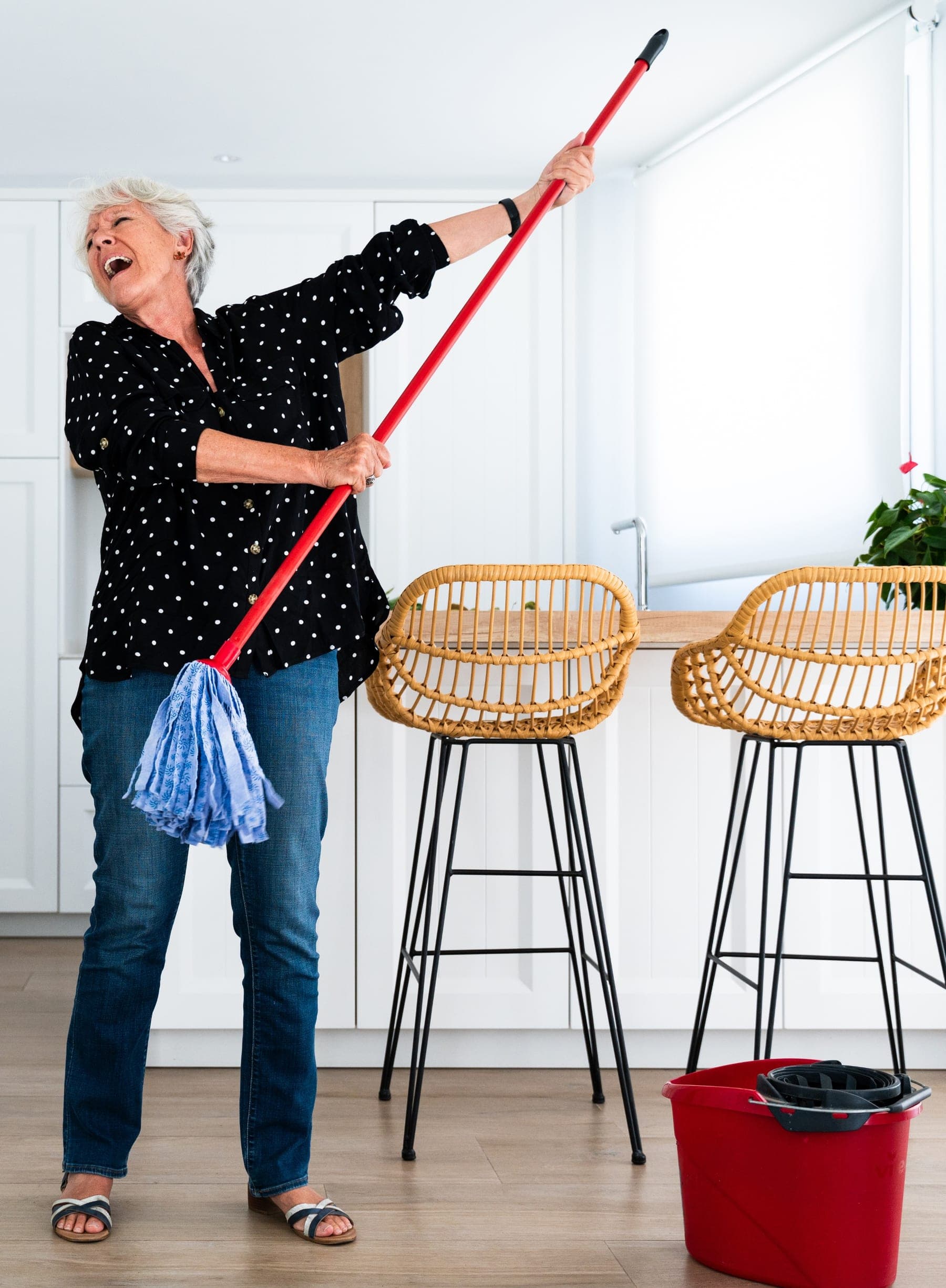 Eine Seniorin singt in der Küche in den Stiel ihres Wischmopps
